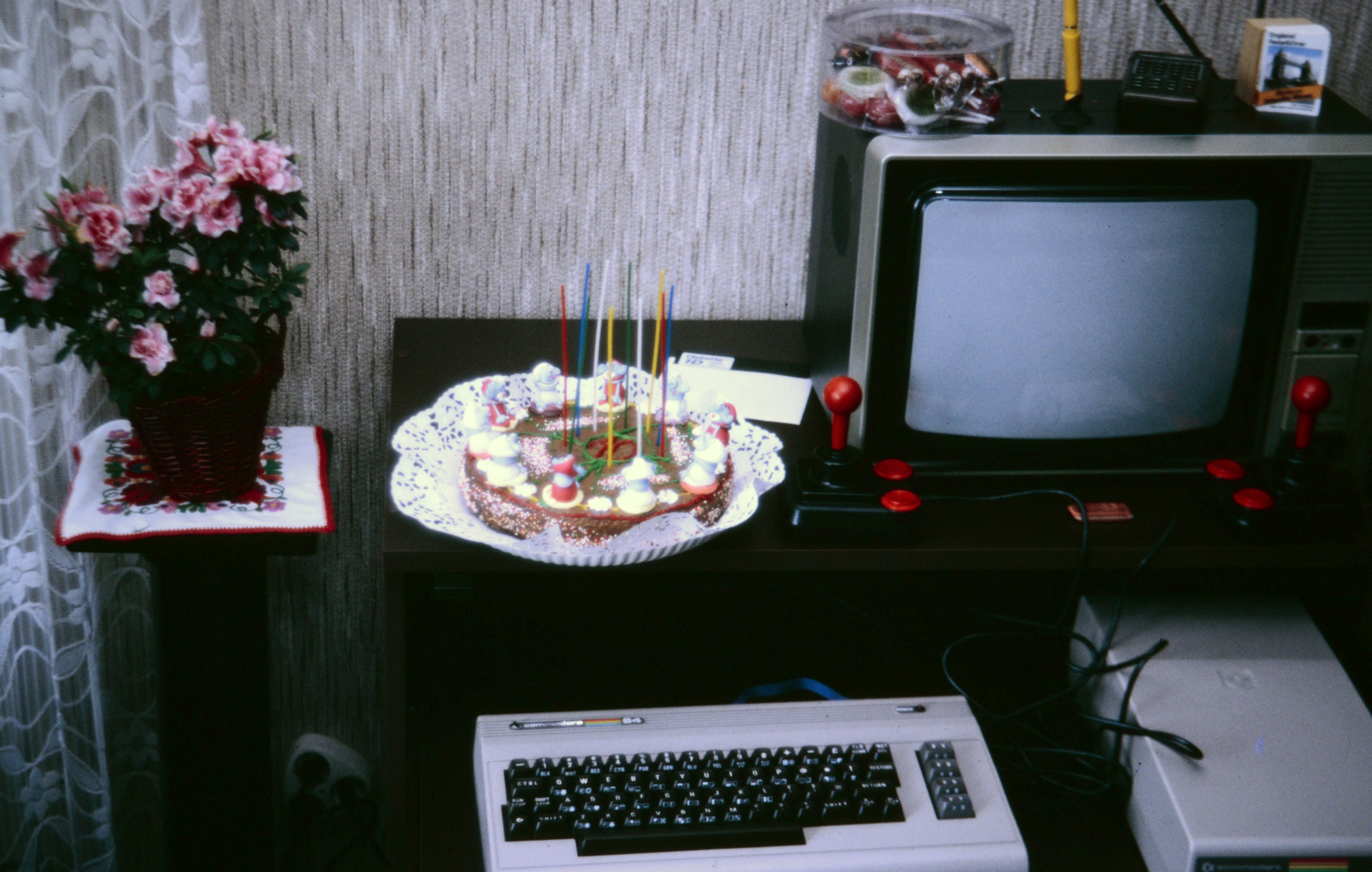 Birthday cake next to a Commodore computer with TV monitor and red joystick, March 1989