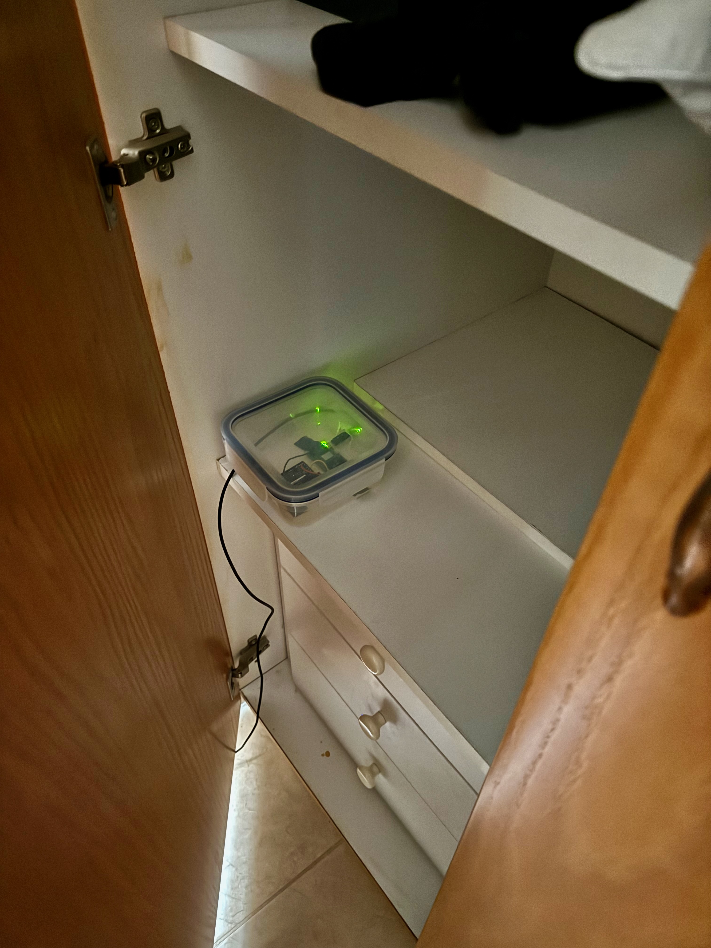 The closed Tupperware in a cupboard with a green LED glowing through the lid