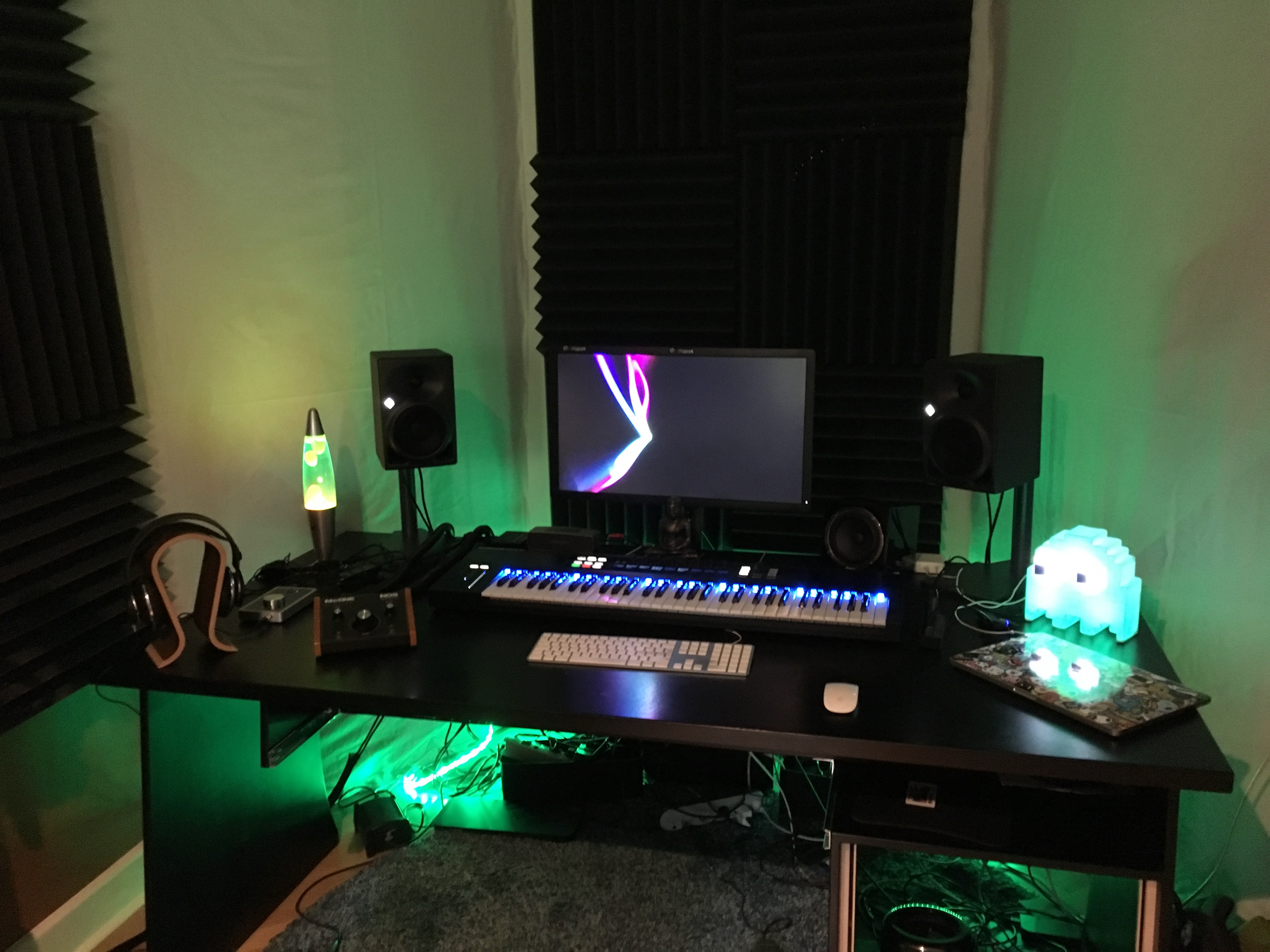 Home studio setup with studio monitors, MIDI keyboard, acoustic treatment, and green LED lighting